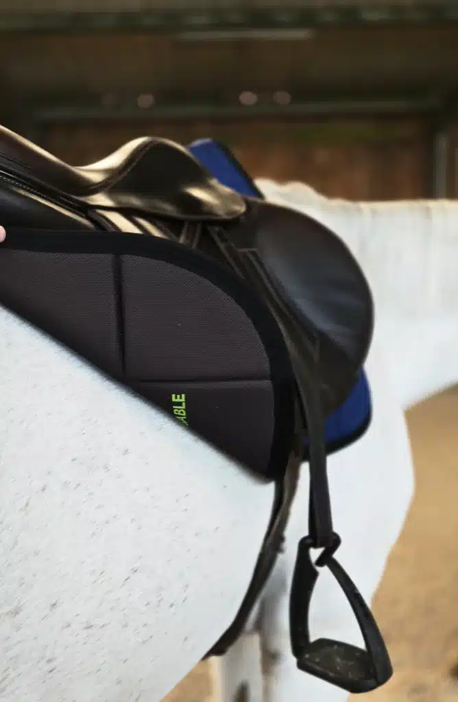 Zoom sur un tapis de selle EliteRide noir et ergonomique, équipé sous une selle d'équitation.